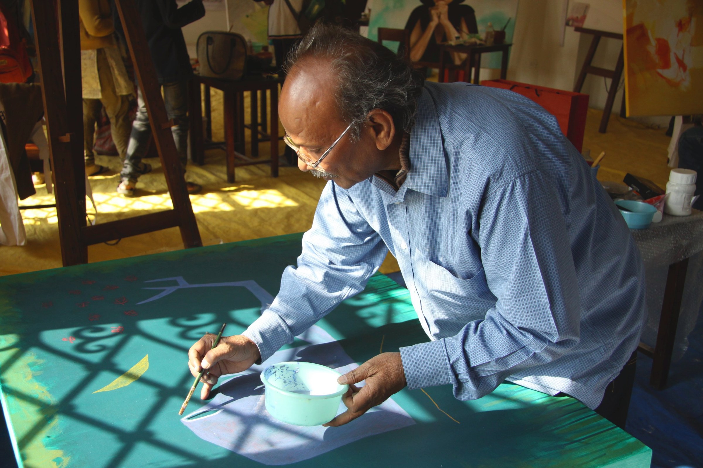 Jai Zharotia painting a large green canvas, a window’s lattice shadow falling across it