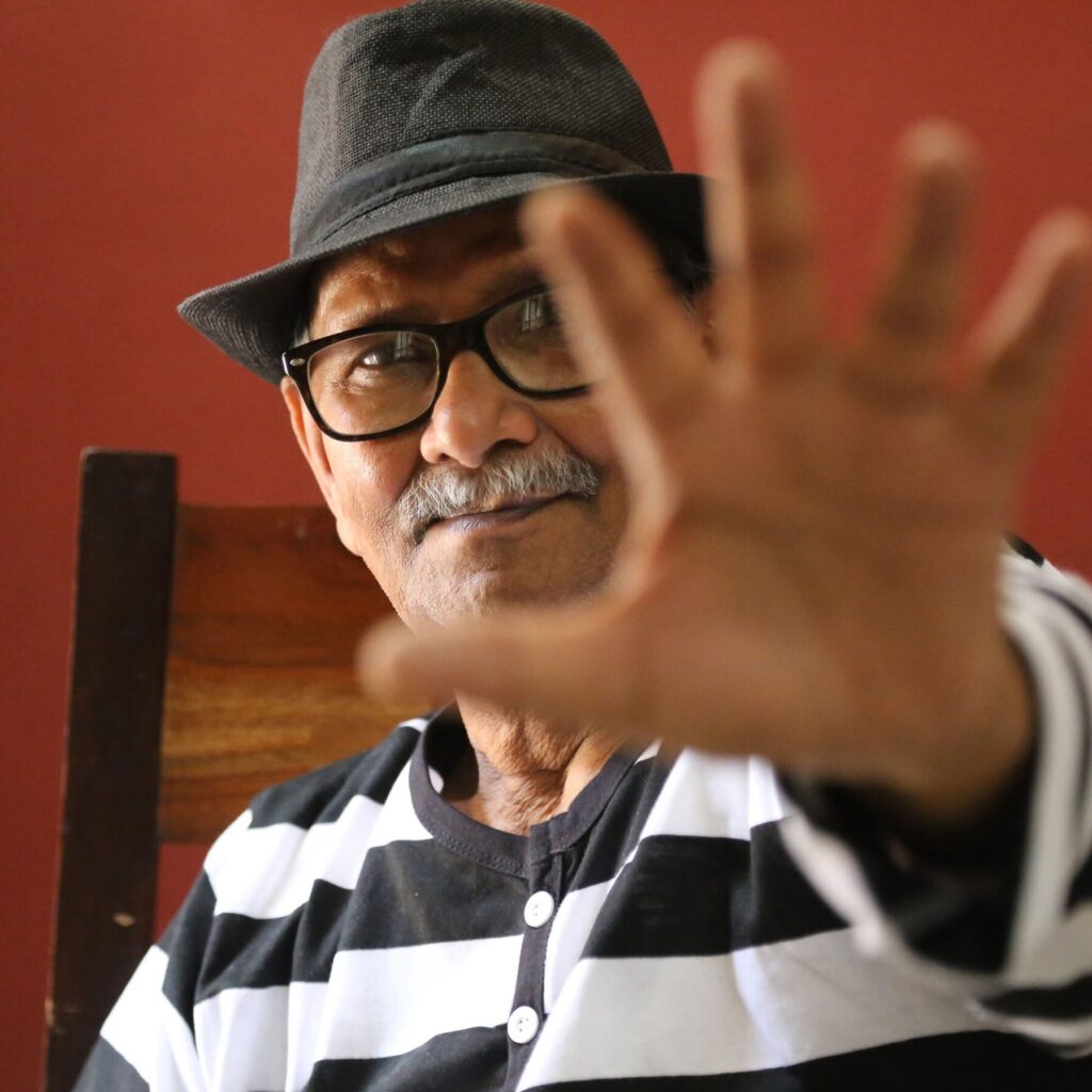 Portrait of Jai Zharotia in a hat, his raised hand half-covering the camera